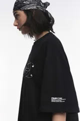 Remera blanca de corte boxy, cuello redondo a la base y mangas cortas. Presenta un pequeño estampado localizado en el centro del pecho que simula un ají en tono rojizo.