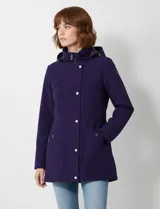 Gabardina impermeable de mujer, color morado oscuro, con capucha desmontable y cierre frontal oculto con botones a presión. Presenta bolsillos delanteros y ajuste interno en la cintura.