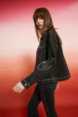 Campera de jean con lavado oscuro rojizo/marrón, estilo trucker. Presenta tachas doradas a lo largo de los bordes de los bolsillos, el canesú y los puños. Posee un bordado en relieve de diseño floral en la manga.