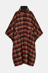 Capa oversize de corte amplio con estampado de cuadros en tonos rojos, negros y marrones. Presenta cuello alto, cierre frontal con botones, bolsillos delanteros y mangas ajustables mediante trabillas con botones.