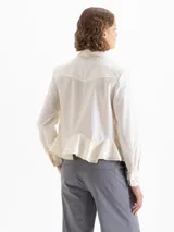 Camisa blanca de popelina con ajuste al cuerpo, puños anchos, cuello de puntas largas, broches dorados y doble volado en la cintura.