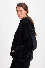 Campera de terciopelo color chocolate, con corte holgado, mangas murciélago y capucha desmontable. Presenta cierre frontal con botones a presión y bolsillos laterales.