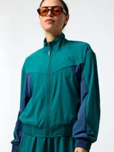 Campera cortaviento de microfibra oversize verde con inserciones azul marino en los costados y mangas, cuello alto y cierre frontal con cremallera.