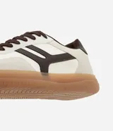 Championes de estilo urbano con diseño retro, confeccionados en material sintético color crema con detalles en marrón oscuro. Presentan recortes laterales, cierre con cordones y suela de goma color caramelo.