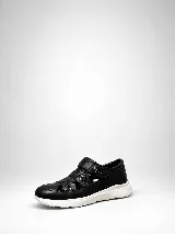 Zapato cerrado tipo zapatilla de cuero natural negro, combinando sectores lisos y texturados, con aperturas laterales y cierre de velcro. Cuenta con suela blanca liviana y anatómica.