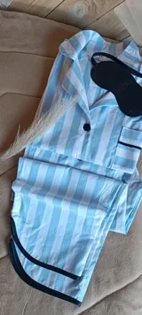 Conjunto de pijama de algodón a rayas celestes y blancas, compuesto por camisa de manga larga con cuello y pantalón largo. Incluye antifaz negro.