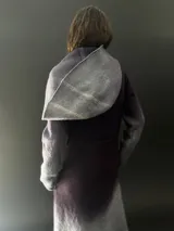 Tapado largo de lana merino color gris oscuro con teñido degradado en gris claro en ruedo, mangas y capucha. Tiene corte recto, bolsillos laterales y cierre cruzado con broches a presión ocultos en los hombros.