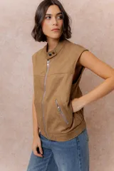 Chaleco de gamuza color marrón con acabado aterciopelado, cuello alto con broche a presión, cierre frontal metálico y bolsillos laterales con cierre.