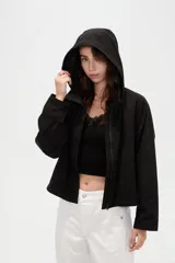 Campera corta de nylon en color negro, con cuello alto, capucha integrada y cierre frontal oculto con solapa.