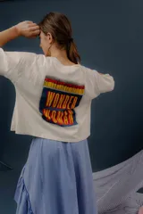 Remera crop de algodón color blanco, de manga corta y calce holgado, con estampa trasera colorida inspirada en cerillas con el texto 'Wonder Woman'.