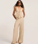 Blusa beige texturizada de corte halter con escote en V, lazo frontal ajustable en el busto y ruedo asimétrico ondulado.