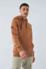 Buzo de algodón color marrón con capucha, bolsillo tipo canguro, mangas largas y logo estampado en el pecho.