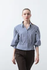 Camisa a rayas azules y blancas de manga larga, con cuello clásico y puños abotonados. Presenta un diseño entallado en la cintura.