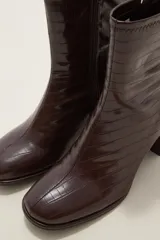 Bota corta de caña media en color negro, confeccionada en eco cuero con acabado brillante. Presenta cierre lateral interno, costura central decorativa en el empeine y taco cuadrado de altura media.