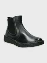 Bota corta de cuero negro tipo chelsea, con paneles elásticos laterales y suela gruesa con costuras visibles.