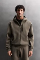 Sudadera con capucha de entrenamiento, confeccionada en tejido técnico de algodón con efecto neopreno. Presenta cierre frontal de cremallera, cuello subido, bolsillos laterales y un bolsillo en el pecho, todos con cierre de cremallera y acabado termofijado.