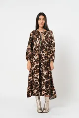 Vestido midi de corte holgado con estampado animal print en tonos marrones y beige. Tiene cuello redondo con lazo, mangas largas abullonadas y falda amplia con volantes. Incluye cinturón marrón con tachas.