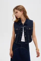 Chaleco de denim azul oscuro con bolsillos con solapa en el pecho, cierres decorativos y cierre frontal con botones metálicos.
