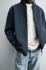 Cazadora bomber ligera de tejido técnico color verde oliva, con cuello, puños y bajo en rib elástico. Presenta cierre frontal de cremallera y bolsillos de vivo en la cadera.