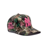 Gorro trucker con estampado de camuflaje de bosque, visera curva y cierre trasero ajustable. Presenta un aplique bordado en relieve con las letras "NY" en color fucsia en el centro, acompañado de los textos bordados "Mi Casa" y "Su Casa" a los lados.