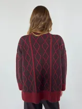 Sweater de lana color bordó con cuello alto y diseño de rombos y líneas verticales en rojo. Tiene puños y dobladillo acanalados.