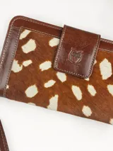 Billetera grande de cuero con detalle de pelo en el frente con estampado tipo animal print de manchas claras sobre fondo marrón, y solapa de cierre con broche y logo de búho grabado.