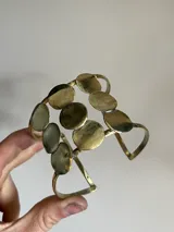 Brazalete rígido de bronce dorado con apliques circulares.