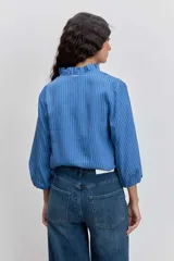 Camisa de manga larga con diseño a rayas verticales en tonos azules. Presenta un cuello mao con detalle de volados a lo largo de la abertura frontal y mangas abullonadas con puños elásticos.