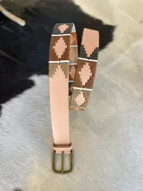 Cinturón de cuero en tono tostado con bordado a mano de hilos encerados en tonos marrones y beige con motivos geométricos, y hebilla metálica rectangular.