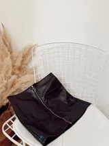 Minifalda negra de ecocuero con cierre metálico frontal y dos bolsillos delanteros.