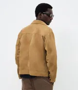 Campera estilo Harrington con diseño trucker, confeccionada en gamuza sintética color tostado. Presenta cuello clásico, cierre frontal por cremallera, bolsillos delanteros con solapa y mangas largas.