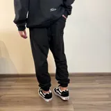 Pantalón tipo jogger de algodón color beige, con puños elásticos en los tobillos y estampa pequeña en el frente con el texto 'BUENA VIBRA EST. 2018'.