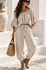 Blusa color beige confeccionada en lino, de diseño holgado y corto con cuello redondo elastizado que permite usarla estilo off-shoulder. Cuenta con mangas anchas y acampanadas con volados en capas.