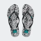 Ojotas Reef Seaside Prints con base negra y estampado de flores blancas, tiras negras con logo Reef en celeste.