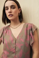 Blusa sin mangas con estampado de hojas rosas sobre fondo marrón, con escote en V y botones al frente. Presenta volados en los hombros y tejido de viscosa liviano.