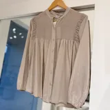 Camisa de manga larga color beige, con cuello mao, fruncidos en el pecho y los hombros, y cierre frontal de botones.