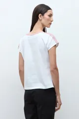 Remera blanca de algodón con escote en V y detalles de bordado étnico en tonos rojizos y naranjas en el cuello y los hombros. De corte recto y manga corta.