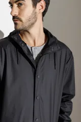 Campera impermeable verde con capucha, cierre frontal con botones a presión y bolsillos laterales con solapa.