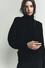Jersey de punto liso color negro, con cuello subido y mangas largas de diseño murciélago con sisa ancha que se estrecha hacia la muñeca.