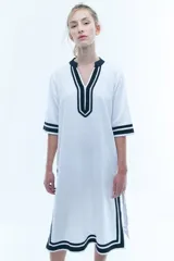 Túnica blanca de corte recto con cuello en V y mangas 3/4. Presenta detalles de ribete negro en cuello, mangas y ruedo.