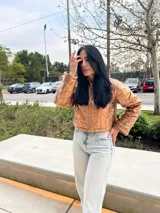 Campera corta color ocre, con cuello alto, cierre frontal con cremallera y diseño acolchado.