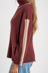 Polera de punto con calce oversize, cuello alto y mangas largas. Presenta un diseño en color negro con franjas laterales en las mangas y detalle en el cuello en tono bronce con acabado brillante.