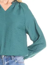 Blusa de satén color verde petróleo, con escote en V y cuello decorado con mostacillas bordadas. Presenta mangas largas con puños elásticos y ruedo también elastizado, brindando un ajuste cómodo y holgado.