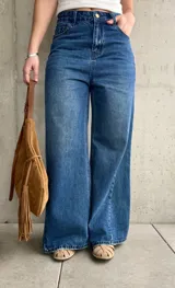 Jean wide leg de tiro medio-alto, color azul con lavado clásico y efecto desgastado. Presenta costuras laterales destacadas que estilizan la silueta, bolsillos delanteros y traseros, y cierre frontal con botón metálico y cremallera.