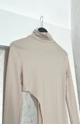 Top largo de cuello alto y manga larga con diseño asimétrico que presenta una abertura lateral pronunciada en la cintura.