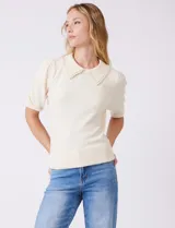 Buzo tejido color beige, marca Nanette, con cuello a la base y solapa decorada con apliques de perlas. Tiene manga corta con puño y ruedo acanalado.