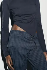 Camiseta de cuello barco y manga larga con diseño asimétrico en el bajo. Presenta un corte entallado con cierre lateral mediante cremallera oculta.