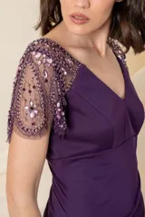 Vestido largo de fiesta color violeta, con cuerpo de jersey y falda de gasa con diseño drapeado y sobrecapa. Presenta escote en V y mangas cortas de tul bordado con pedrería al tono.