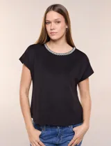 Blusa de silueta recta confeccionada en crepe elastizado, color negro, con escote a la base destacado con una delicada tira aplicada de perlas y cuentas, mangas cortas dollman y ruedo recto.