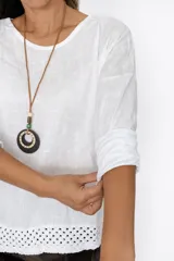 Remera blanca de manga larga con cuello redondo y detalle de tejido crochet en el dobladillo. Incluye un collar fino dorado como accesorio.